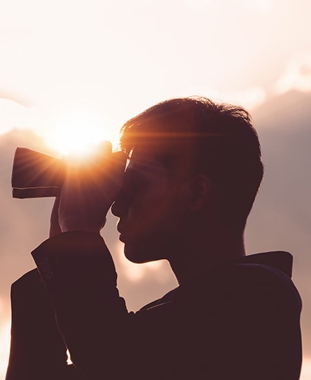 Silhouette of man looking through binoculars at sunset.