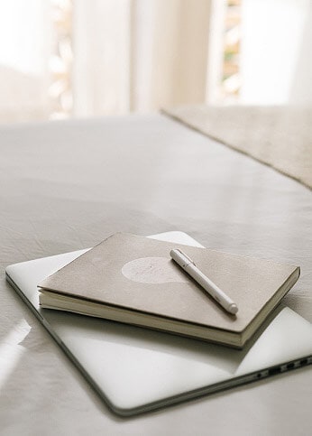 A pen and a notebook on top of a laptop on a table.