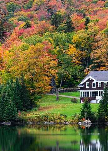 A house is reflected on the surface of a lake in New England during the fall season.