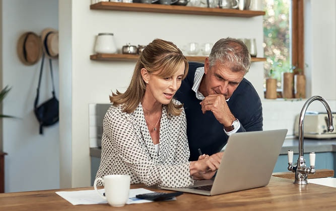 Middle-aged couple looking at a laptop in their kitchen.