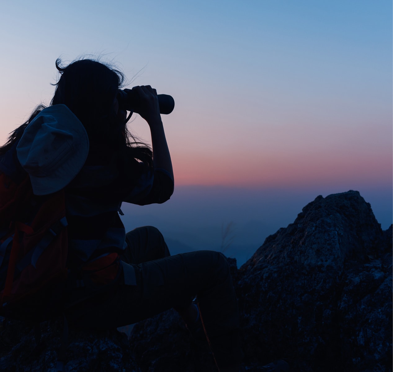 Woman looking through binoculars at twilight.