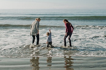 Grandmother, mother, and young child playing in the surf on the beach.