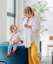 Mother with young daughter sitting on the arm of a chair.