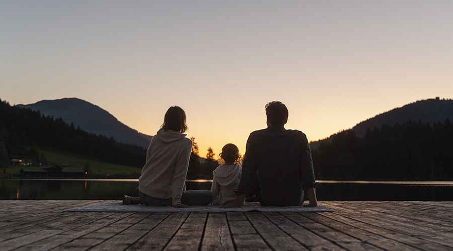 Parents with young child watching sunset on a dock.