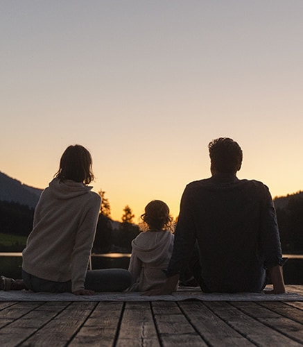 Parents with young child watching sunset on a dock.