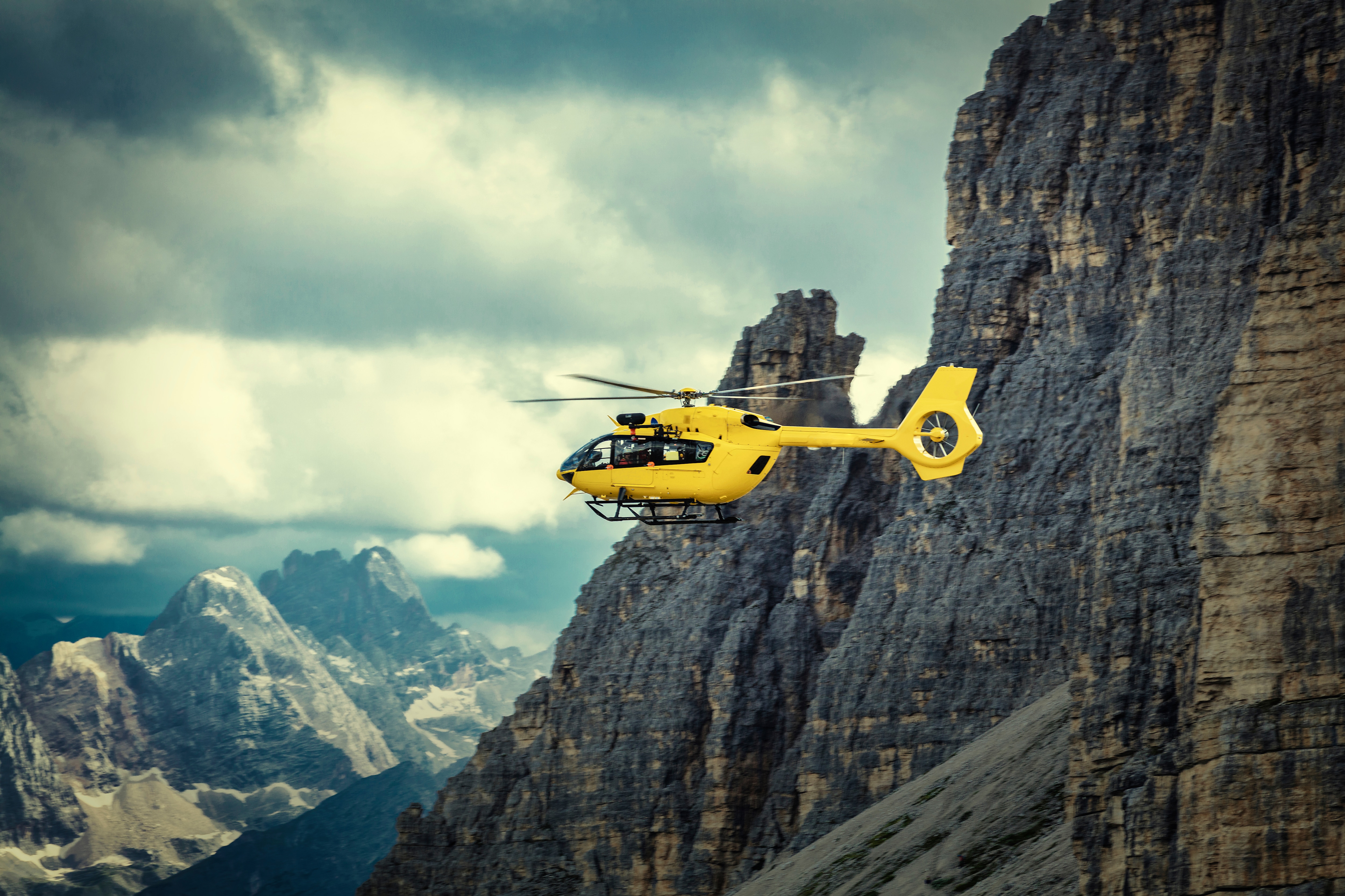 Yellow helicopter flying through mountains