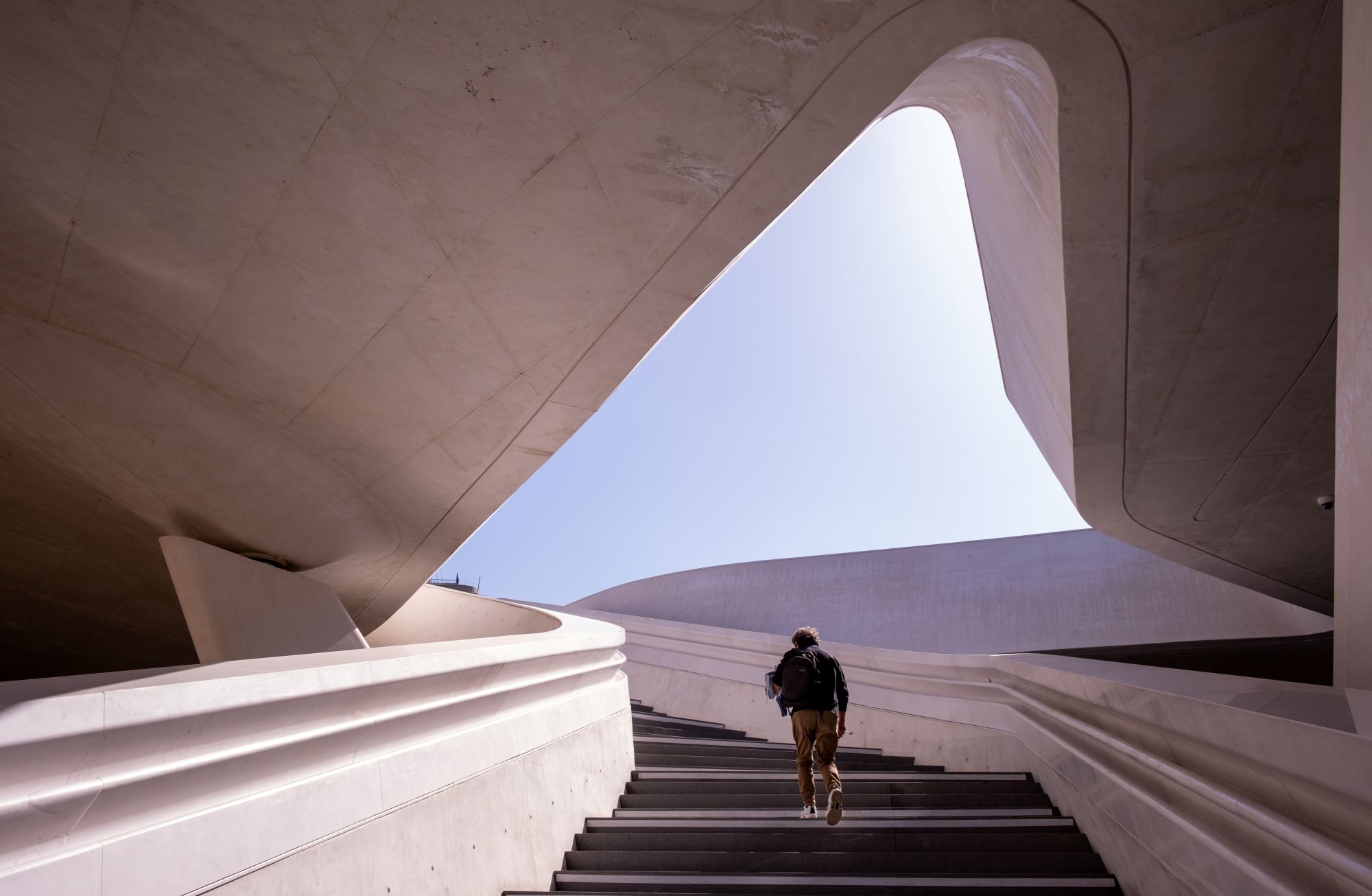 A person walks up the stairs in a concrete building with a curved exit